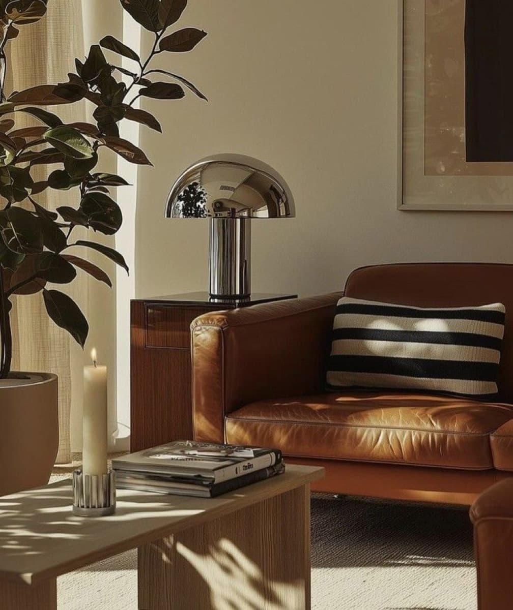 Sala con sofá de piel, lámpara cromada y una planta junto a la ventana
